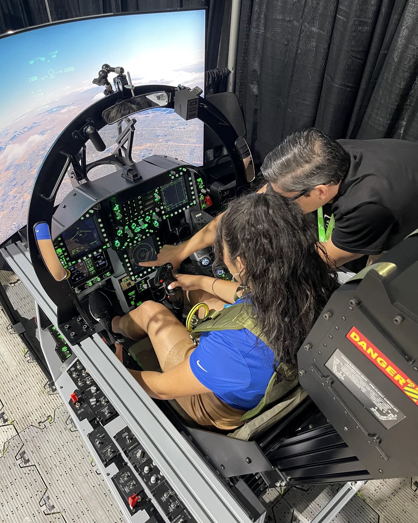 Dogfight Dynamics team member guiding a visitor through the F/A-18C cockpit controls